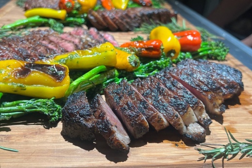 Two sections of sliced steak on a cutting board topped with vegetables.