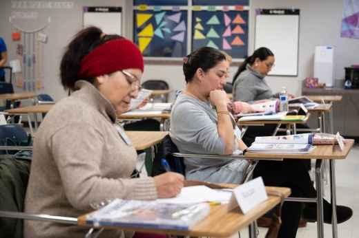 Three adult females sitting in desks in a school classroom.