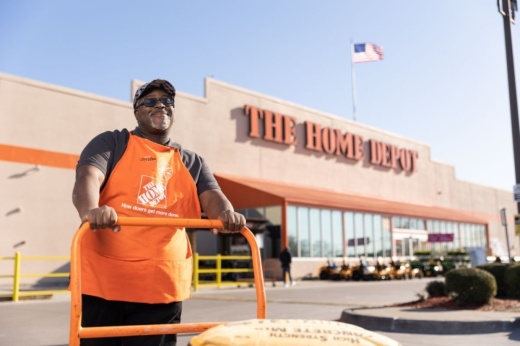 A male employee at The Home Depot pushes a cart outside of a store location.