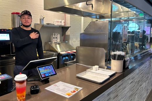 Male standing behind a counter in a food court restaurant.