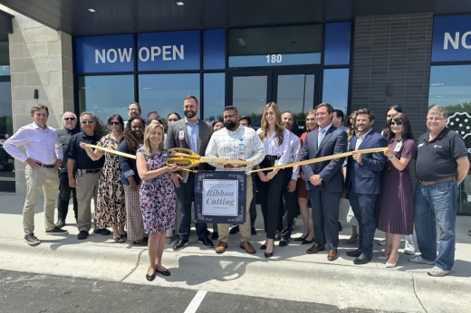 People stand outside a CareNow to cut a ribbon with large scissors