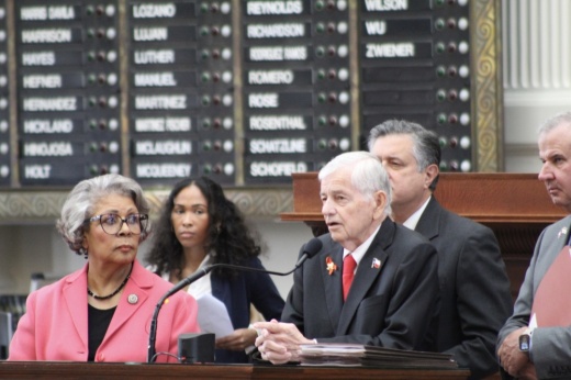 a group of people stand behind a podium on the Texas House floor