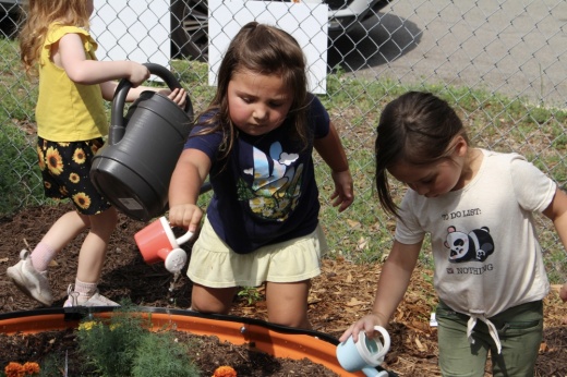 Two children watering a garden bed with watering cans.