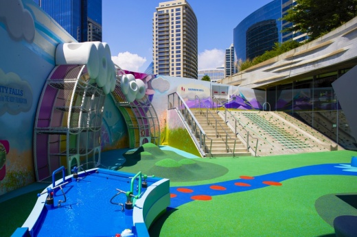 Outdoor play space with water feature, artificial grass and elevated stadium seating.
