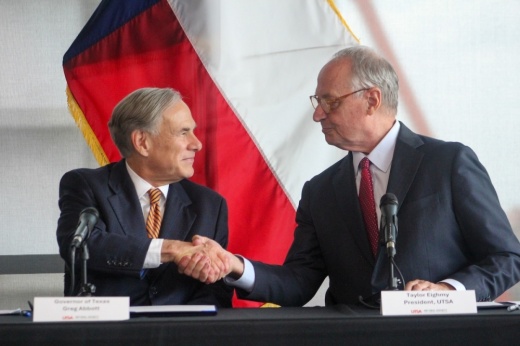 Gov. Greg Abbott and University of Texas at San Antonio President Taylor Eighmy shake hands at a desk in San Antonio.