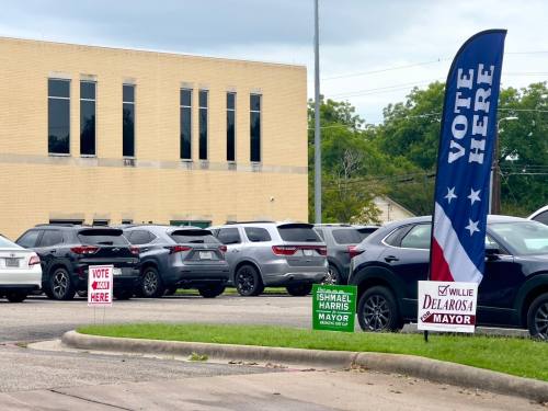 The light brown, brick courthouse is in the background with election signs in the foreground.