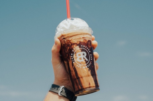 Person's hand holding a frozen coffee featuring Black Rock Coffee Bar branding.