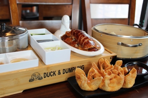 A tray of crispy duck with sides behind a plate of cheese crab puffs on a table at a Chinese restaurant.