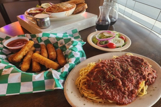 A plate of spaghetti topped with meat sauce, a tray of mozarella sticks, and a bowl of lasagna.