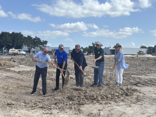 Five team members hold shovels to break ground on a new development site.