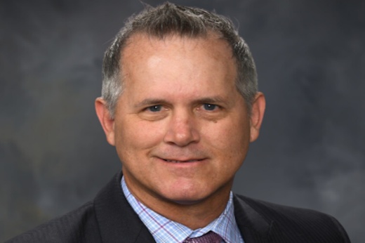 The headshot of an older white man in a black suit is shown to announce his hiring as the chief financial officer of a hospital in San Antonio, Texas.
