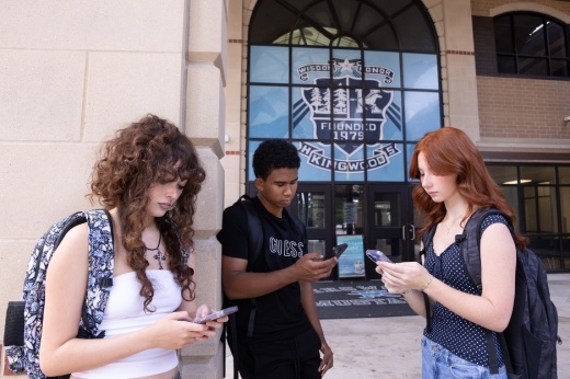 From left, Kingwood High School seniors Sybelle Goff, Donovan Baker and Hania Schmonsees use their cellphones outside before the school day begins. A new Texas law prohibits students from using personal communication devices, including cellphones, during the school day. (Raphael Fernandez/Community Impact)