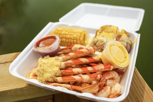 A takeout box with crab, shrimp, corn, potatoes and cajun sauces.