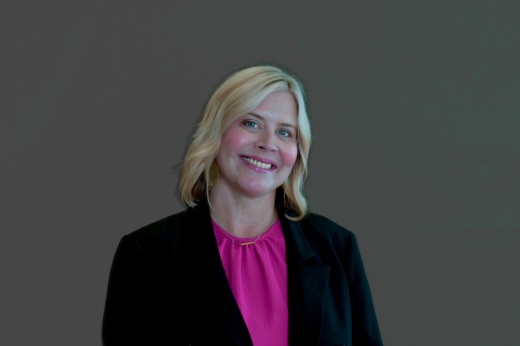 a woman in a pink shirt and black blazer jacket smiles for a photo