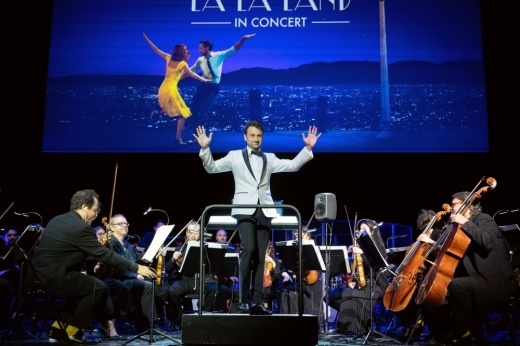 Composer Justin Hurwitz conducts as La La Land plays on the screen behind him during a live concert performance. (Courtesy Lionsgate Films)
