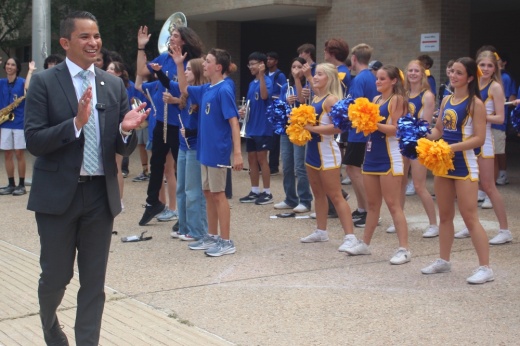 The superintendent claps while watching cheerleaders and band members perform