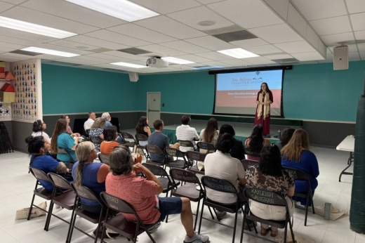 a woman speaks to a group of people in a classroom