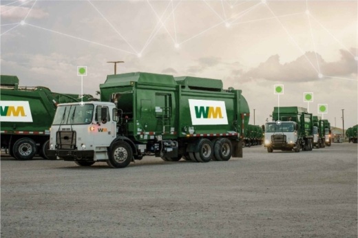Green garbage trucks from Waste Management are seen driving on a partly cloudy day.