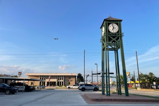 Clock tower in front of Humble City Hall with a plane flying overhead in the distance