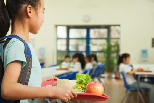 A girl holding a tray of food in a school cafeteria.