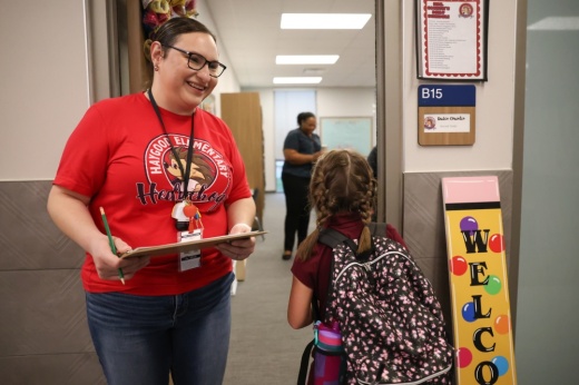 a teacher stands at the classroom door as a student passes by