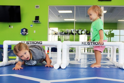 One girl crawling under a hurdle while a younger girl watches.