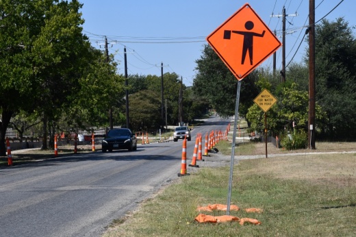 a construction sign and cones in a street lined with trees