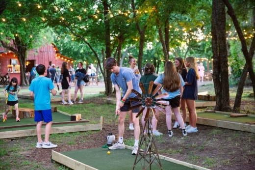 Teens playing mini golf outside under trees.