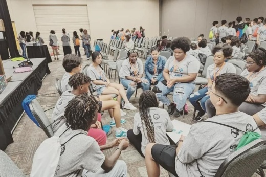 teenagers sit in a group inside a conference room