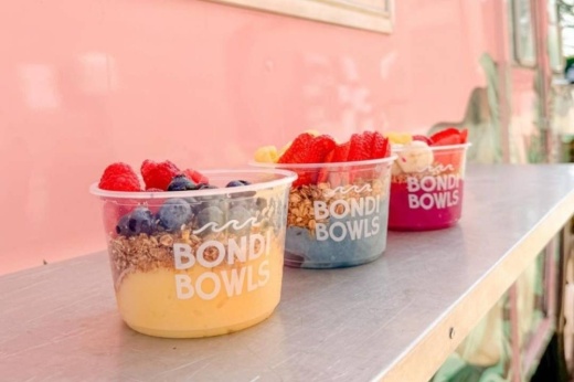 Three bowls filled with layers of smoothie, granola and fruit.