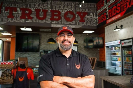 man in a black shirt crosses his arms in front of a wall that reads truboy