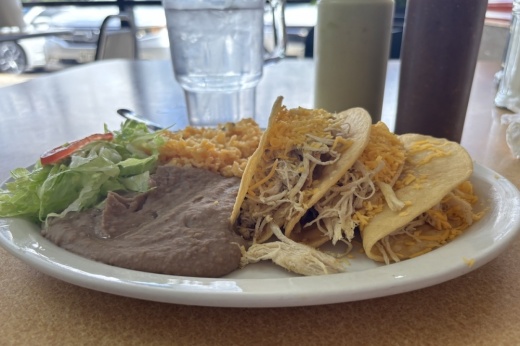 a white plate with crispy tacos and rice and beans
