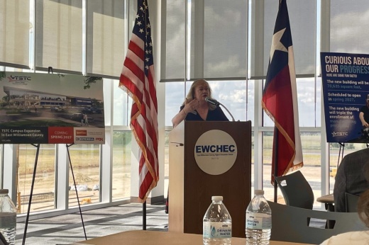 woman speaks at a podium in front of windows