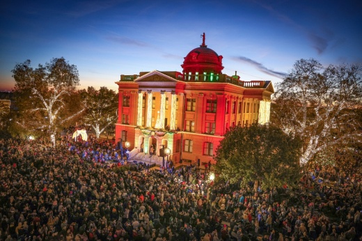 a town courthouse is lit up for the holidays with a crowd gathered in front