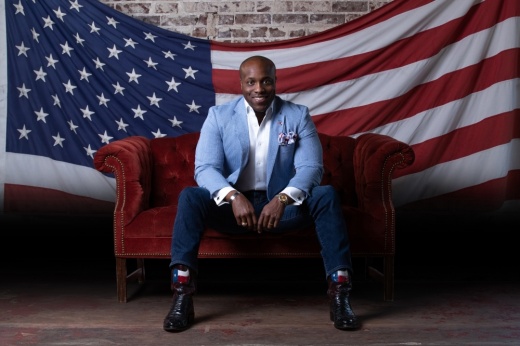 a man sits on a couch in front of an american flag on the wall