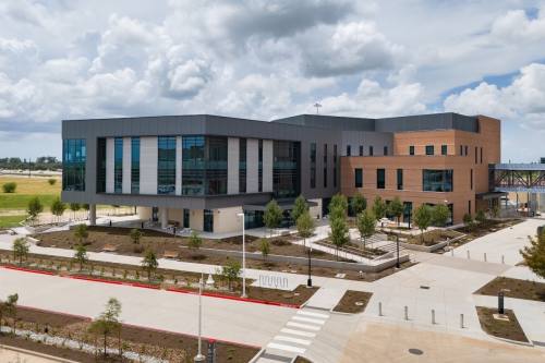 a gray academic building with windows and a sidewalk path below