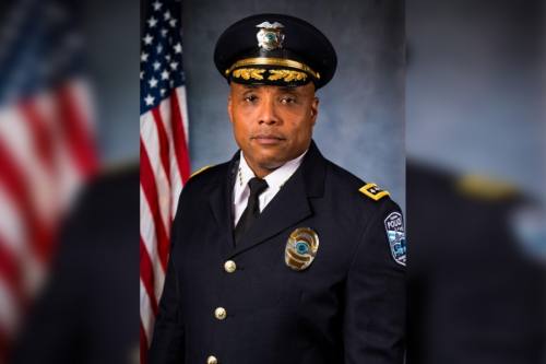 headshot of a man in a formal police uniform in front of american flag