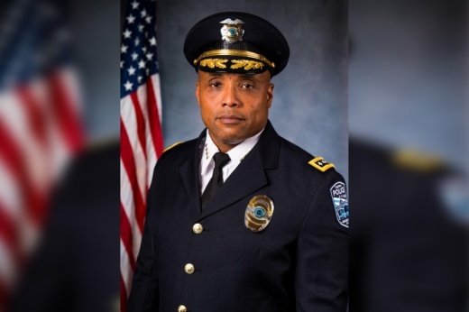 headshot of a man in a formal police uniform in front of american flag