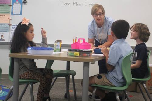 A teacher works with elementary students sitting at a table