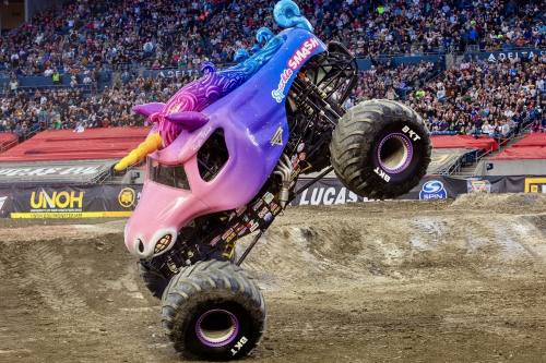a monster truck decorated as a pink and purple unicorn in a dirt arena