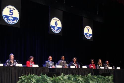 people sit at a long table on a platform with a black curtain in the background