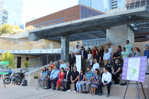 people sit in an outdoor amphitheater and listen to a speaker at a podium