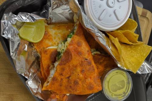 Quesadilla sliced into triangles and served in a to-go box with tortilla chips.