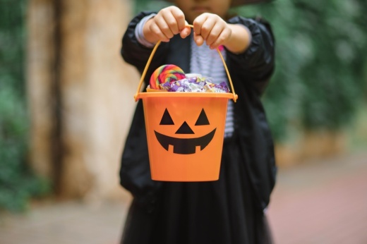 a person holds an orange trick or treat bucket with a jack o lantern face on it