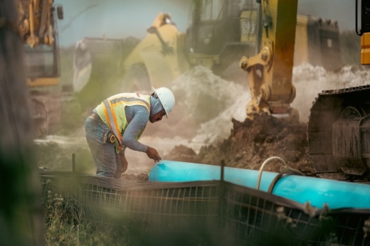 A construction site is shown with a worker tending to a pipeline.