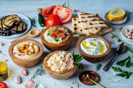 Four dips in bowls with sides of pita bread and tomatoes..