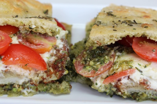 Sandwich on focaccia bread featuring tomato, cheese, chicken and seasoning.