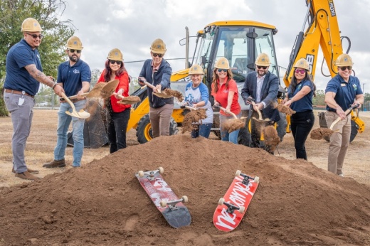 Officials shovel dirt at the groundbreaking. A tractor is in the background and two skateboards rest on the pule of dirt.