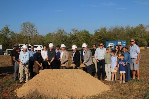 people wearing white hard hats dig shovels into a pile of dirt
