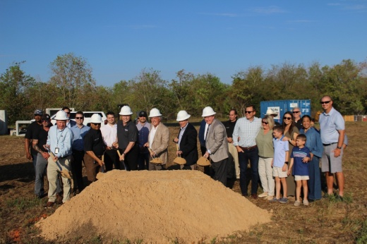 people wearing white hard hats dig shovels into a pile of dirt
